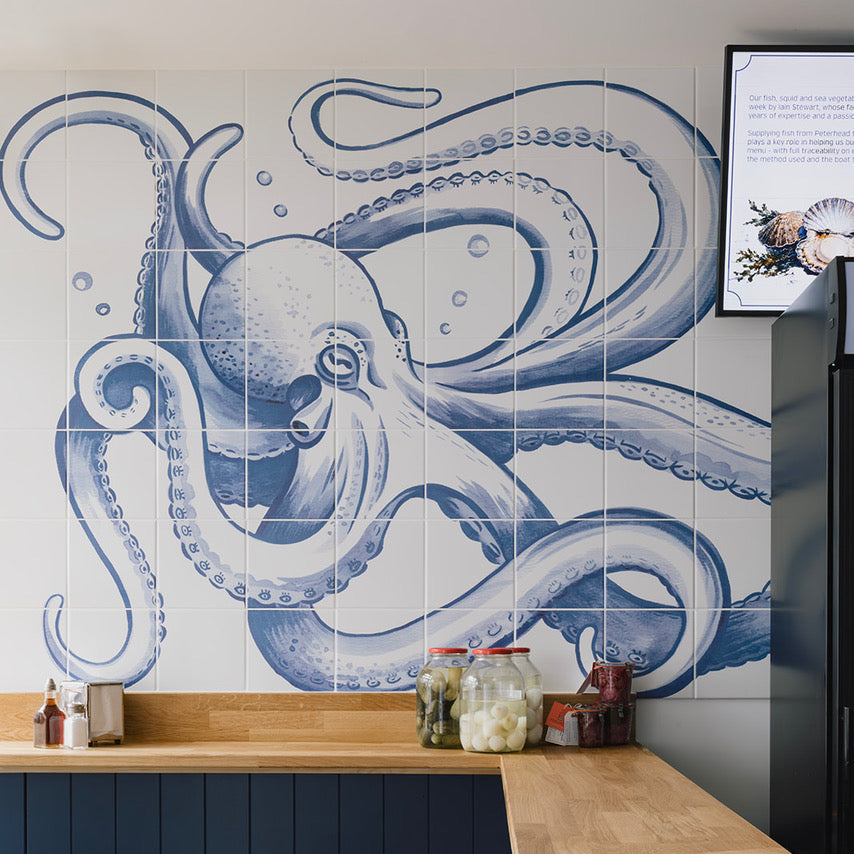 A kitchen interior featuring a large blue octopus mural on a white tiled wall above a curved wooden countertop and dark blue paneled cabinetry.