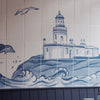 Blue and white tiled wall mural depicting a lighthouse on waves, with a wooden table and navy wainscoting in the foreground.