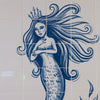 Blue and white ceramic tile mural featuring a mermaid with long flowing hair, a crown, and a scaled tail, with a decorative plant motif in the lower right corner.