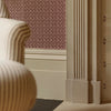 A close-up interior detail showing a cream striped armchair in the foreground, a fluted decorative fire surround, patterned wallpaper, with a dark floor.