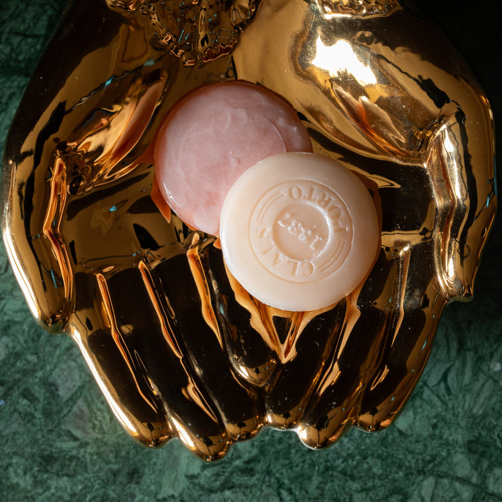 Gold hand shaped dish holding two small round soaps on a green marble surface