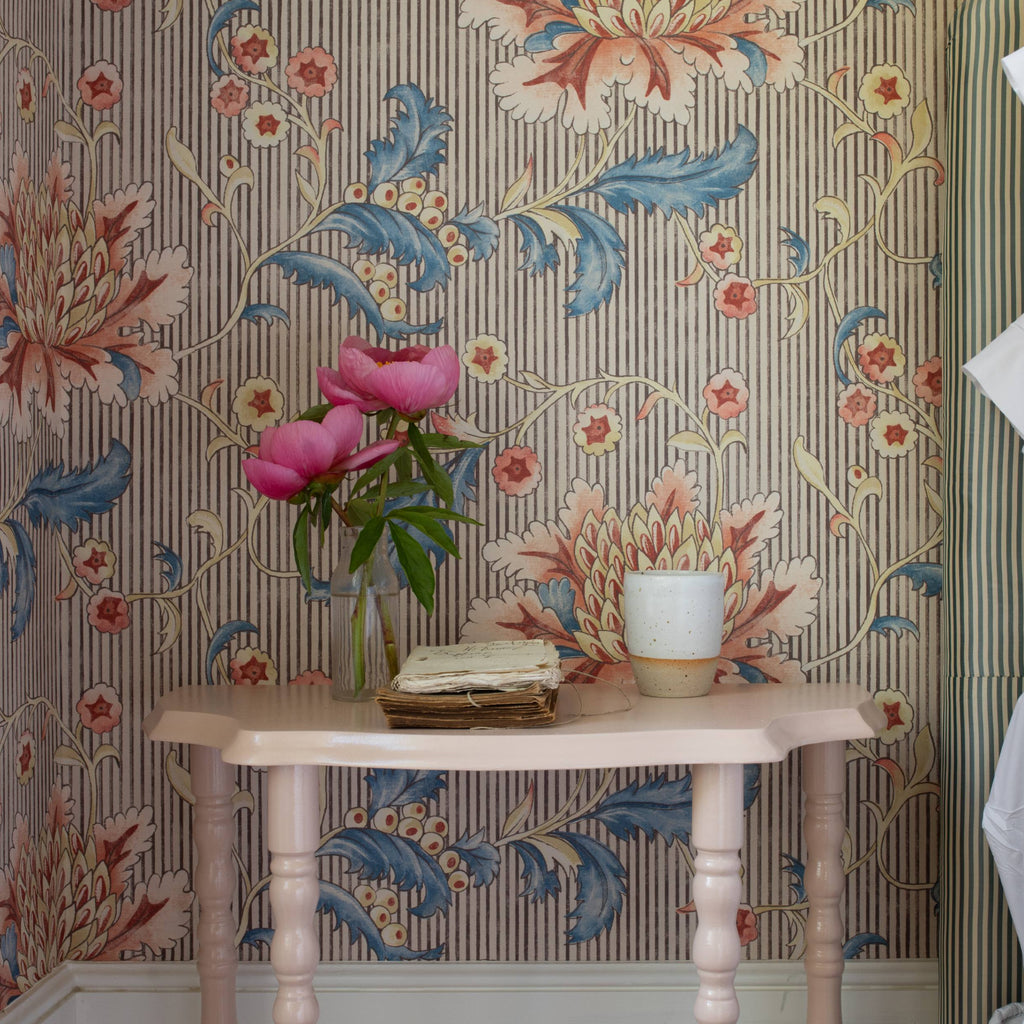 Decorative room with floral wallpaper, pink painted wooden table, and flowers in a vase.