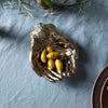 Decorative hand shaped silver dish with olives on a textured blue tablecloth