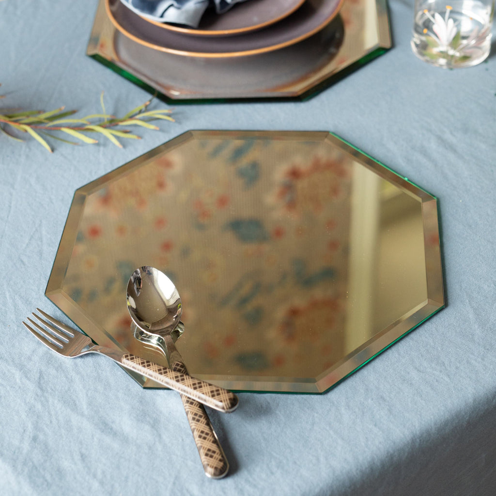 Decorative mirrored hexagonal placemat on a table setting with tartan cutlery and a blue tablecloth.