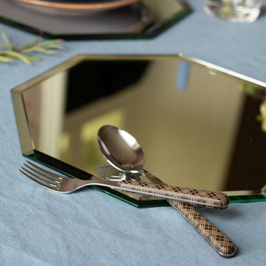 Silver fork and spoon with tartan handles, placed on a mirrored hexagonal placemat.