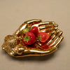 Gold hand-shaped dish with strawberries on a beige background