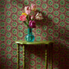Green table with a vase of flowers against a patterned wallpaper wall.