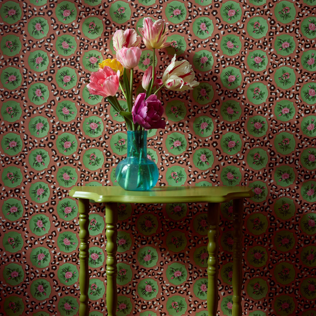 Green table with a vase of flowers against a patterned wallpaper wall.
