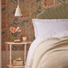 Bedroom with floral wallpaper, bed with white bedding, and side table with decor items.