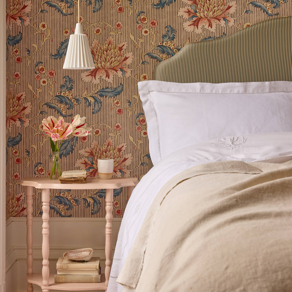 Bedroom with floral wallpaper, bed with white bedding, and side table with decor items.