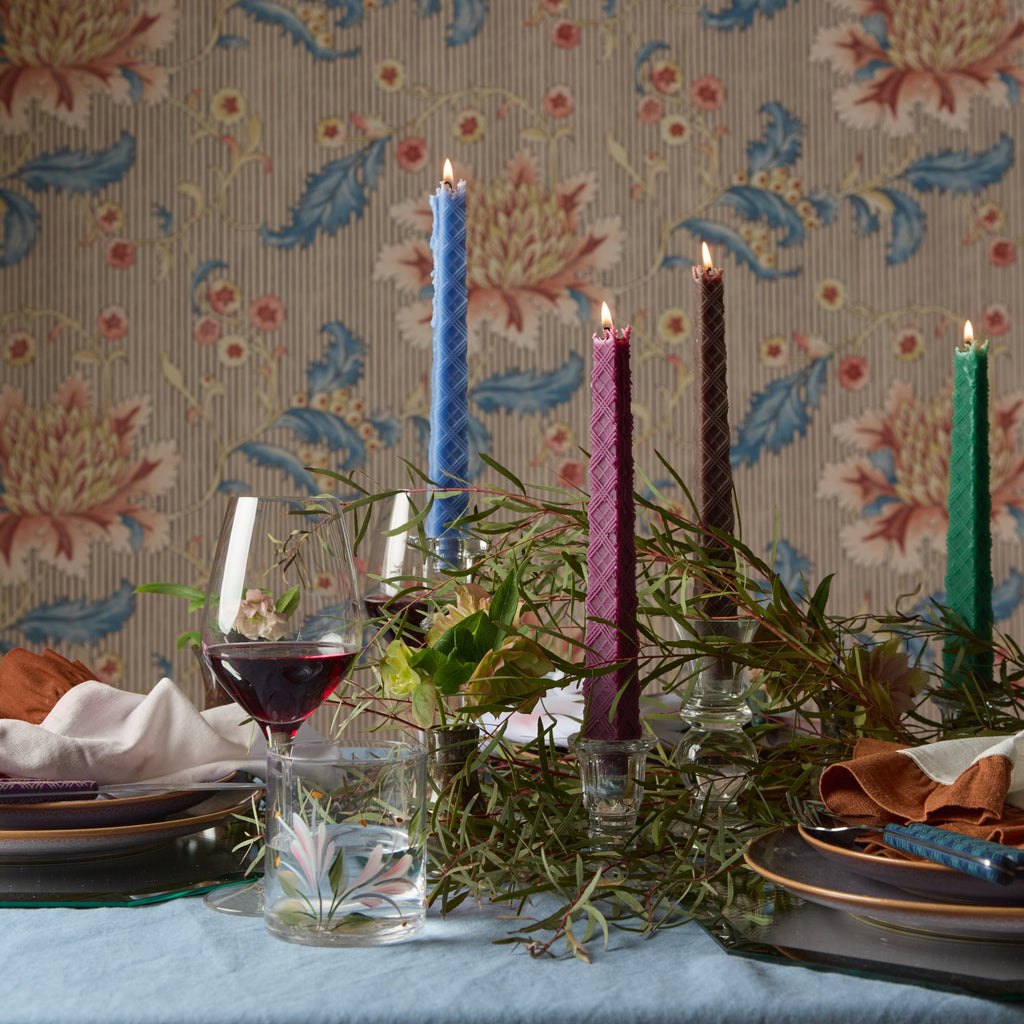 Decorative table setting with candles and greenery against a floral wallpaper background