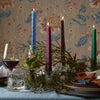 Decorative table setting with candles, greenery, and patterned wallpaper.