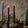 Coloured tartan embossed candles on a table with a fliral wallpaper background. 