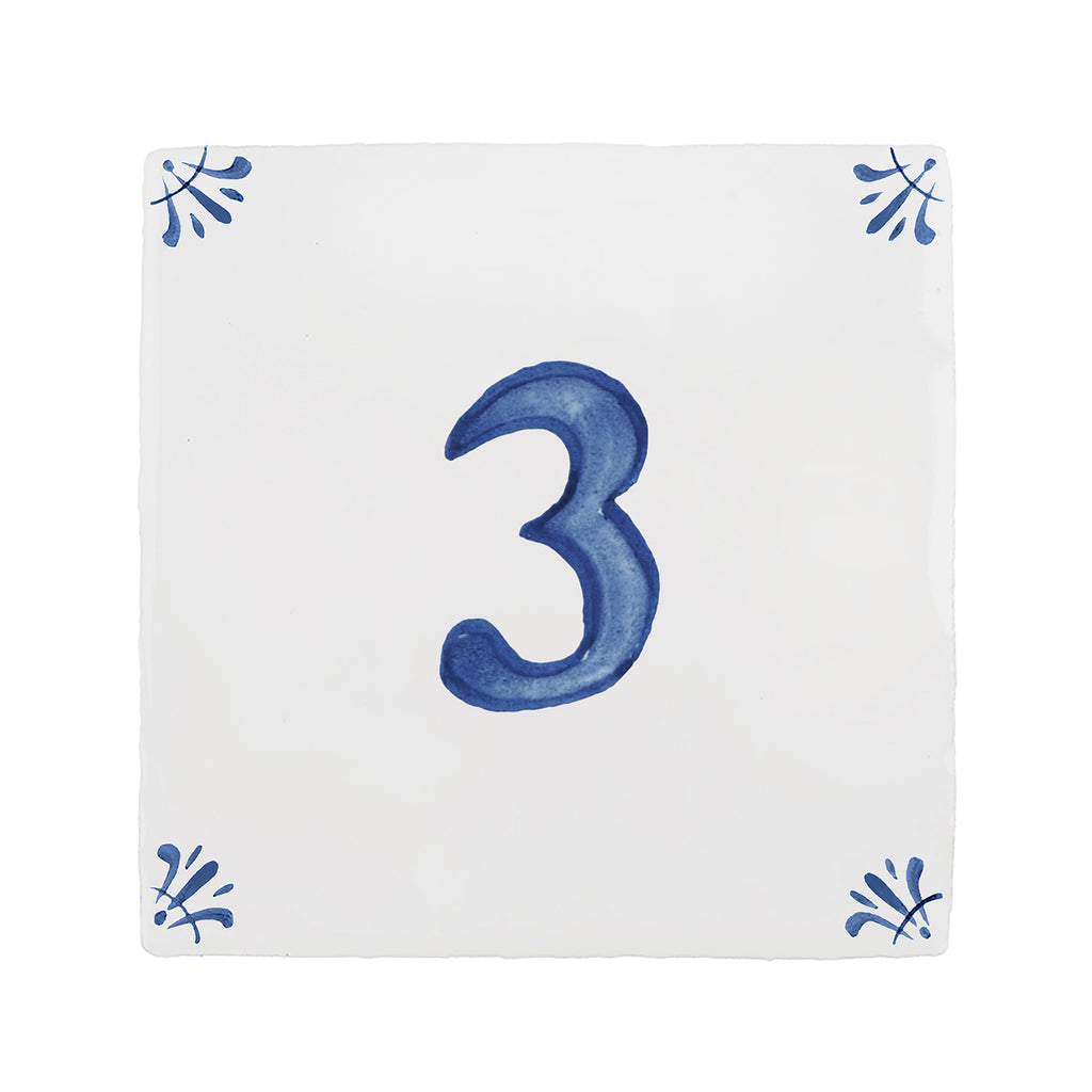 A square white ceramic tile or coaster featuring a large blue painted number 3 in the center, with small blue decorative motifs in each of the four corners.