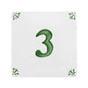 A square white ceramic tile or coaster featuring a hand-painted green number 3 in the center, with small green leafy sprigs in each of the four corners.