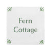 A square white decorative tile or sign with the words 'Fern Cottage' printed in dark green serif text, with small green leaf motifs in each corner, shown on a plain white background.