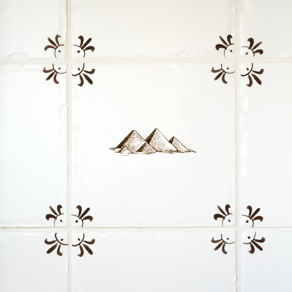 Decorative tile with pyramid design and decorative corners on a tiled wall.