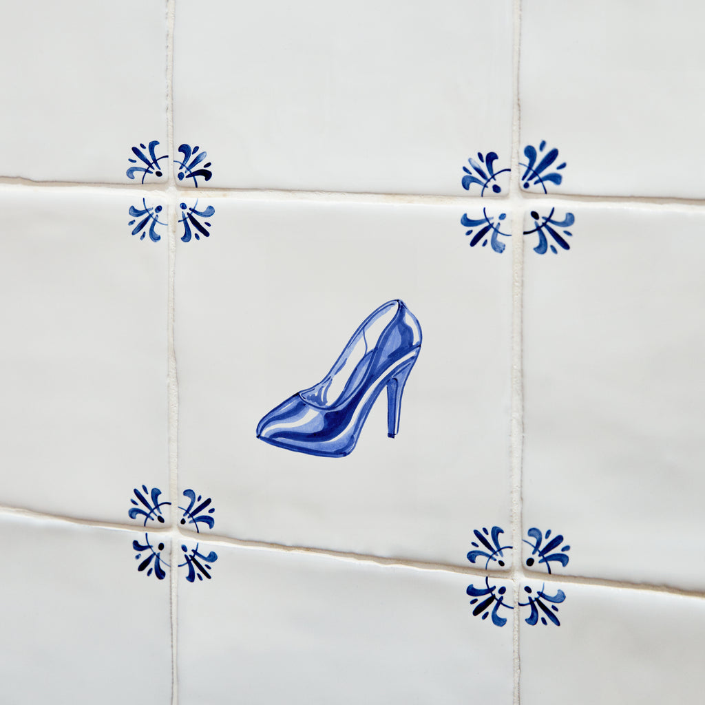Blue high-heeled shoe tile on a tiled wall with decorative blue patterns.