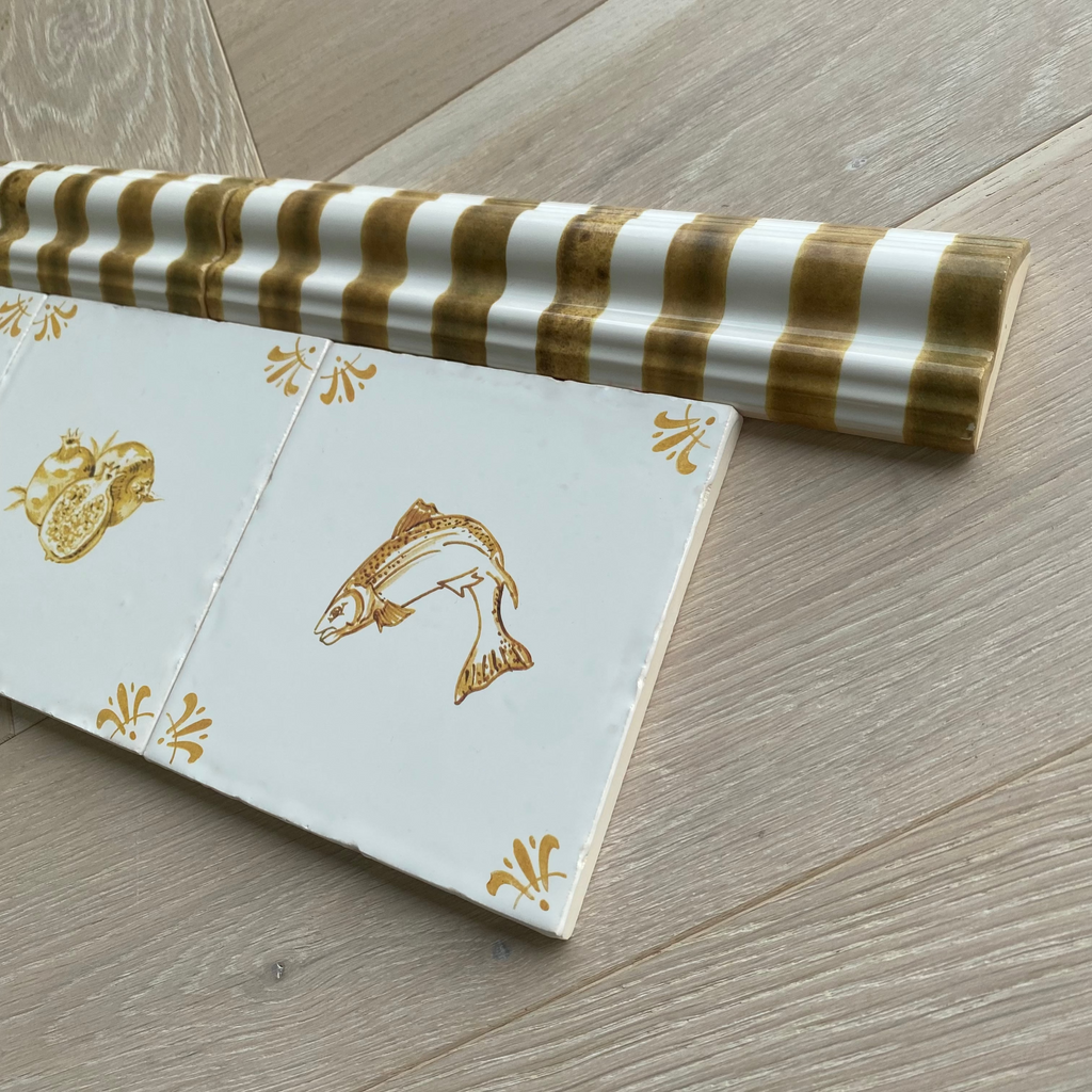 Two striped dado tile trims next to two mustard coloured delft tiles. 