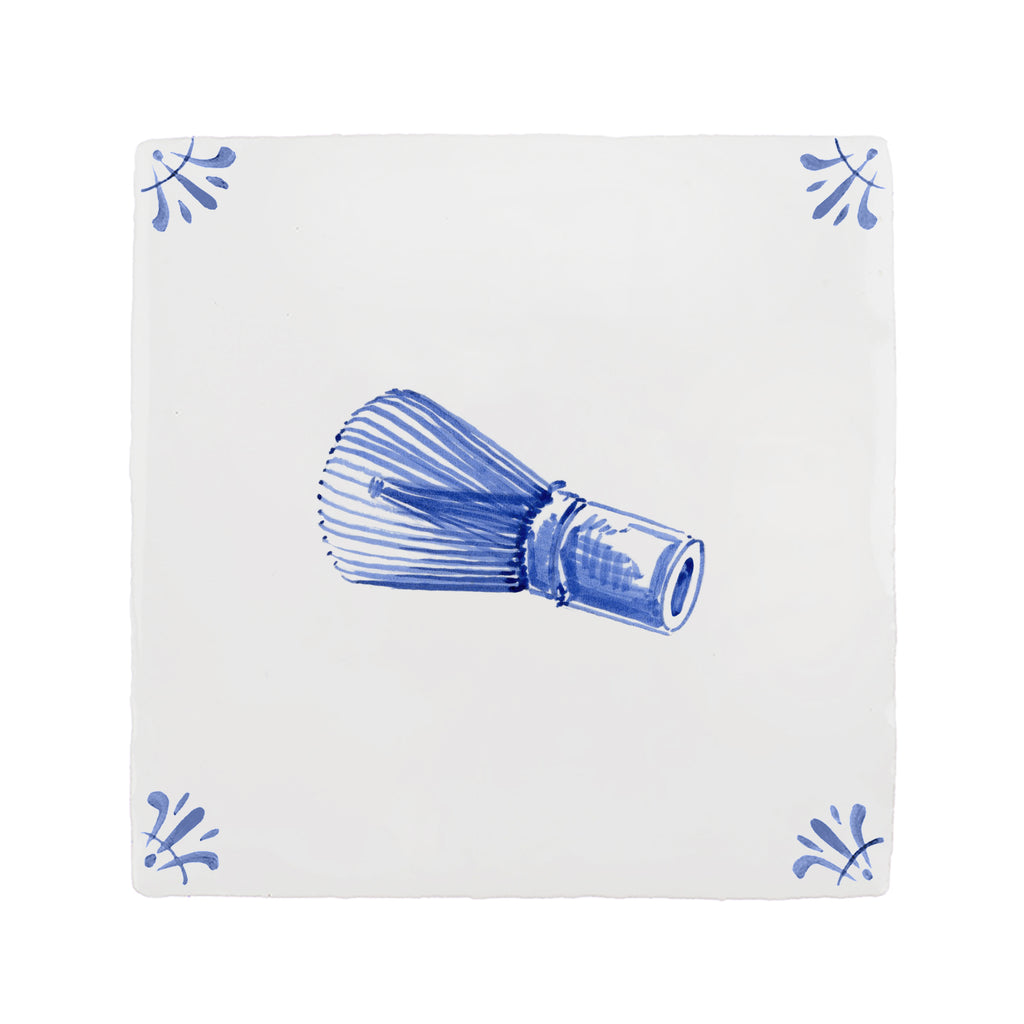 Blue and white matcha whisk on a white tile background with blue decorative corners
