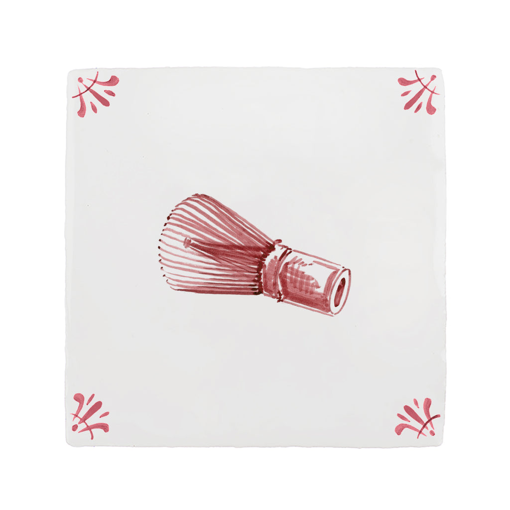 Red matcha whisk on a white tile background with decorative patterns