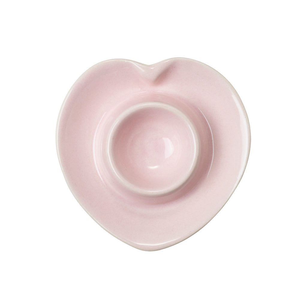 A pink heart shaped ceramic egg cup seen from above on a white background.