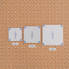 Three square white ceramic tiles with blue floral designs are laid out on a patterned orange wallpaper, comparing the sizes of 10cm, 12.5 and 15cm tiles